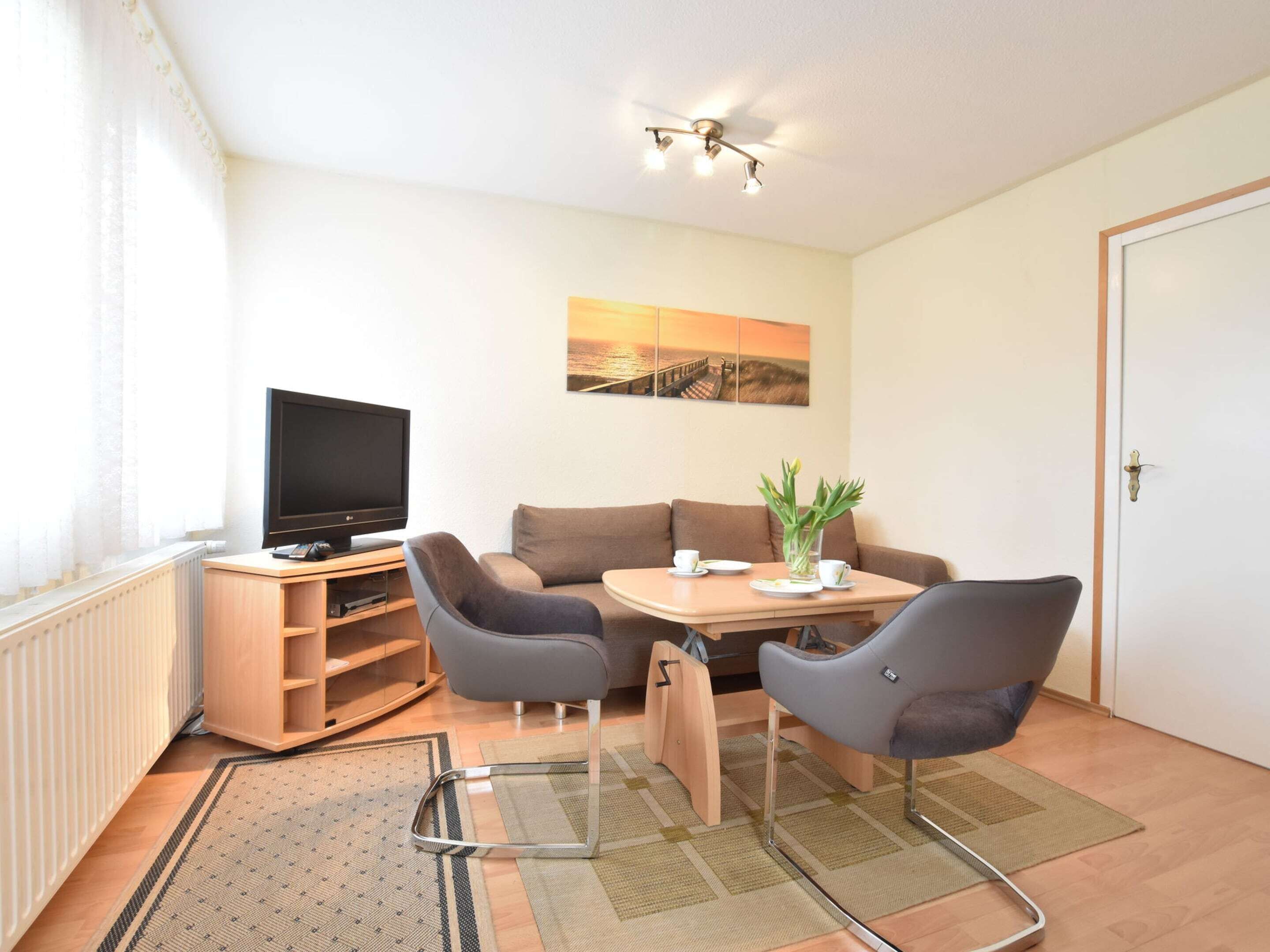 A cozy living room with a flat-screen TV, a sofa, two armchairs, a small table, and a painting on the wall.