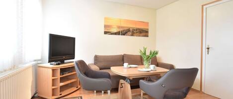 A cozy living room with a flat-screen TV, a sofa, two armchairs, a small table, and a painting on the wall.