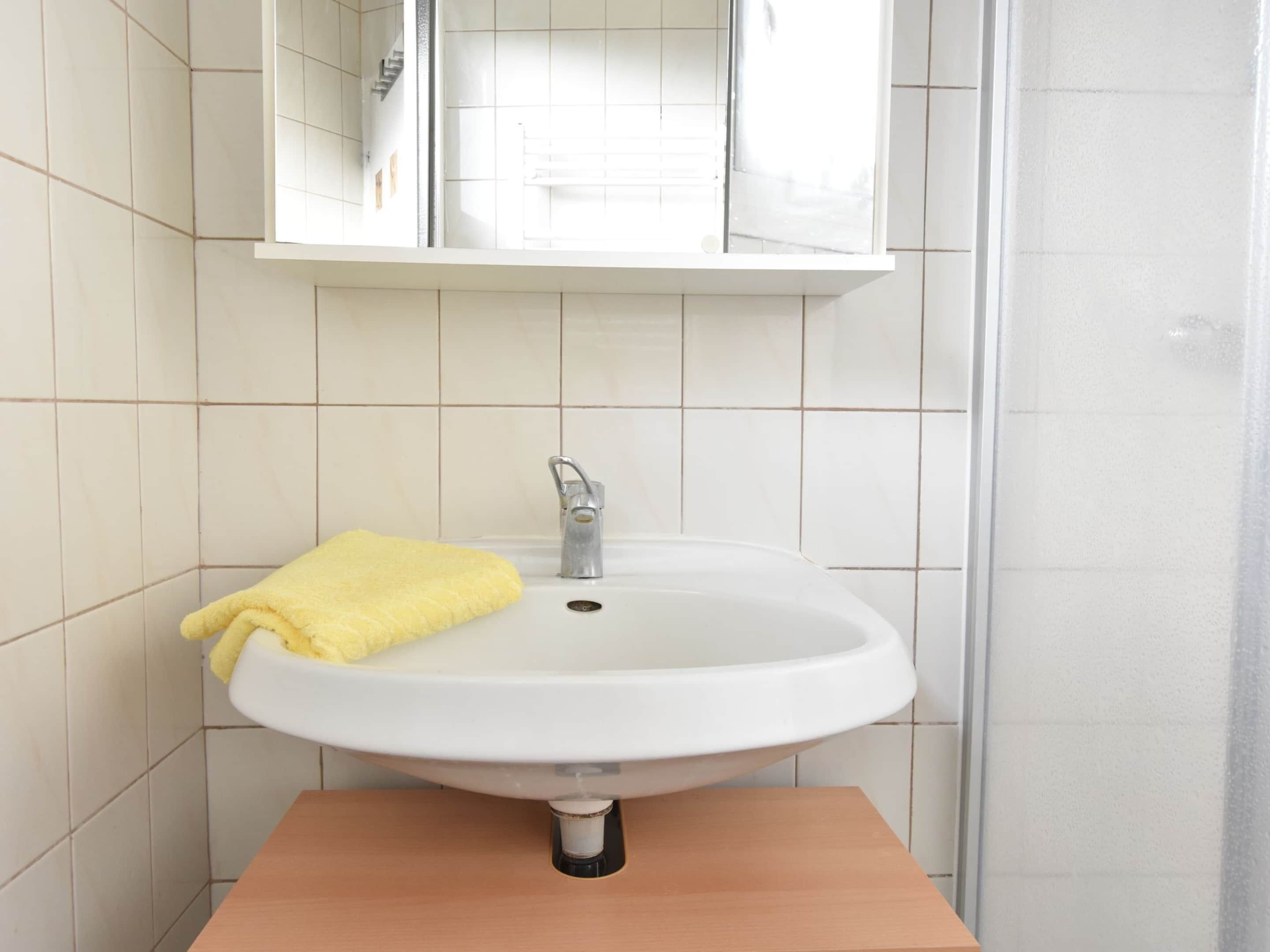 Un baño con un lavamanos blanco, una toalla amarilla y un espejo sobre el lavamanos.