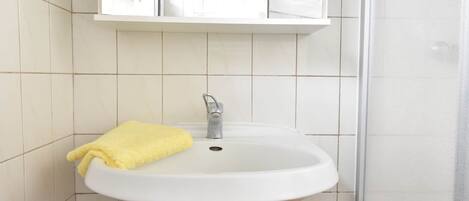 Un baño con un lavamanos blanco, una toalla amarilla y un espejo sobre el lavamanos.