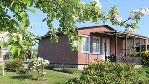 A brick house with a porch, surrounded by a well-maintained garden with flowering plants and a lawn. - Strandbungalow, Boltenhagen (Boltenhagen)