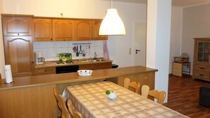 A kitchen with wooden cabinets, a dining table with chairs, and a hanging pendant light. - Geraeumige Ferienwohnung mit Terrasse in Kluetz (Klütz)