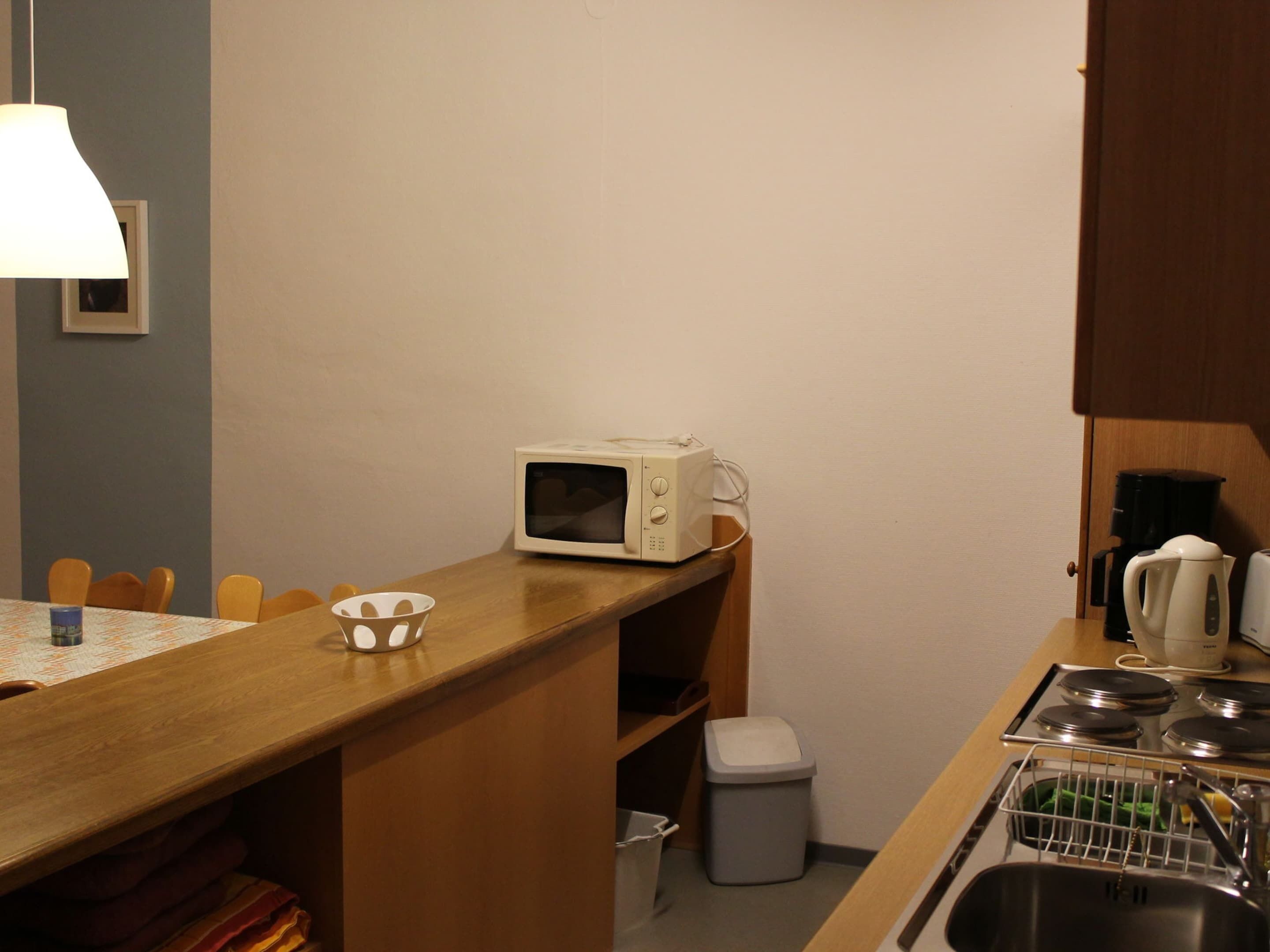 A compact kitchen with a microwave, sink, and a small trash bin.