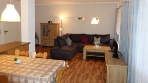 A living room with a sofa, a wooden coffee table, and a dining table with chairs. - Geraeumige Ferienwohnung mit Terrasse in Kluetz (Klütz)