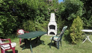 An outdoor seating area with a stone-built fireplace, surrounded by lush greenery.