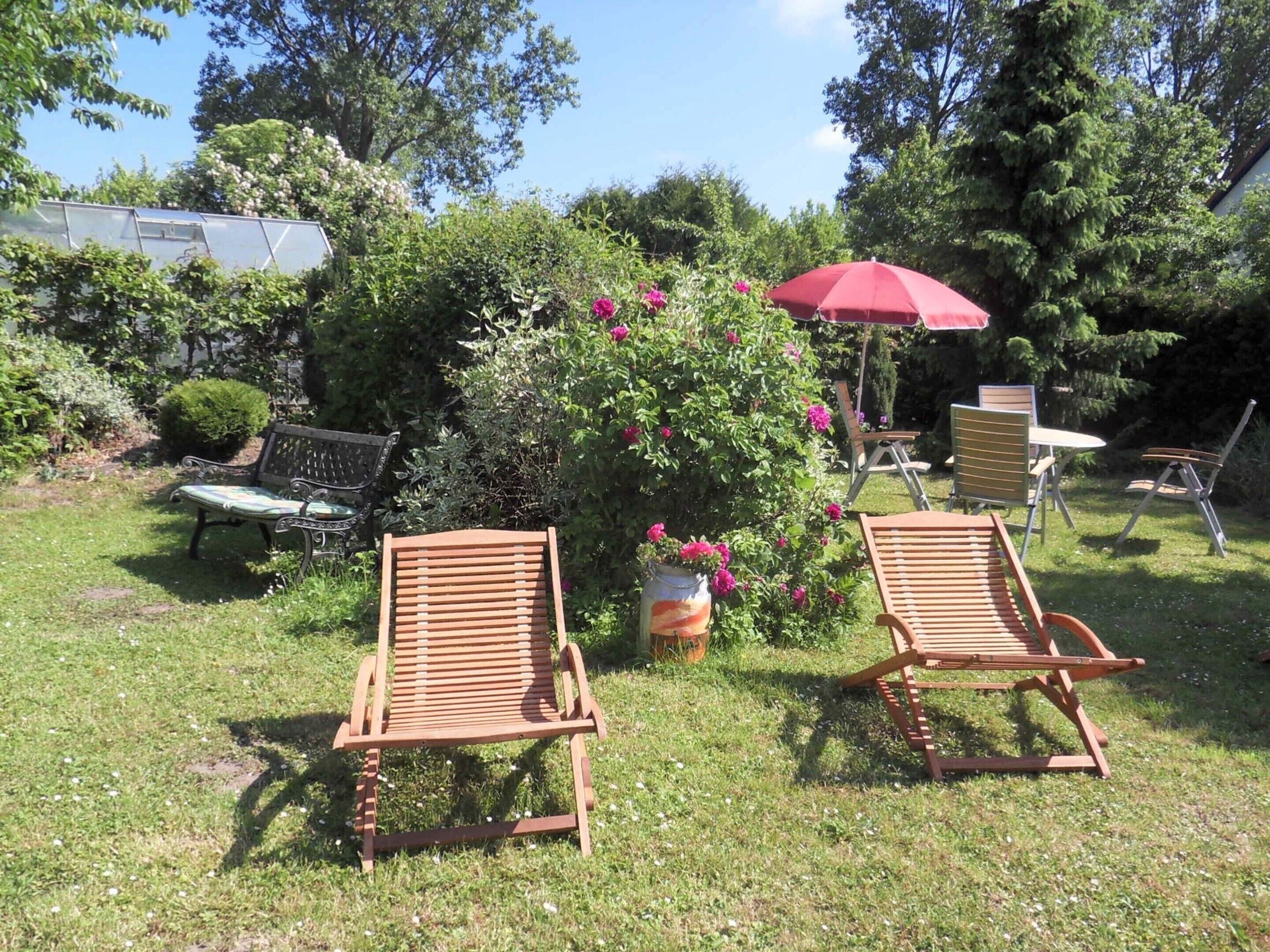 Ein Garten mit zwei Holzliegen, einem roten Sonnenschirm und einer Bank.
