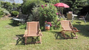 A garden with two wooden lounge chairs, a red umbrella, and a bench.