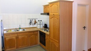 A compact kitchen with wooden cabinets, a built-in oven, and a stainless steel sink. - Wohnung mit Terrasse in Klutz (Klütz)