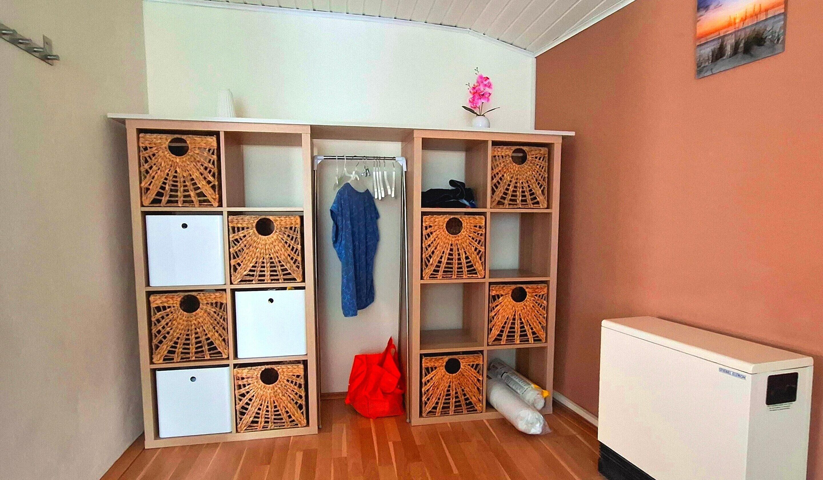 Ein Zimmer mit einem Schrank, der viele Fächer, eine Kleiderstange und einen kleinen Heizkörper beinhaltet.
