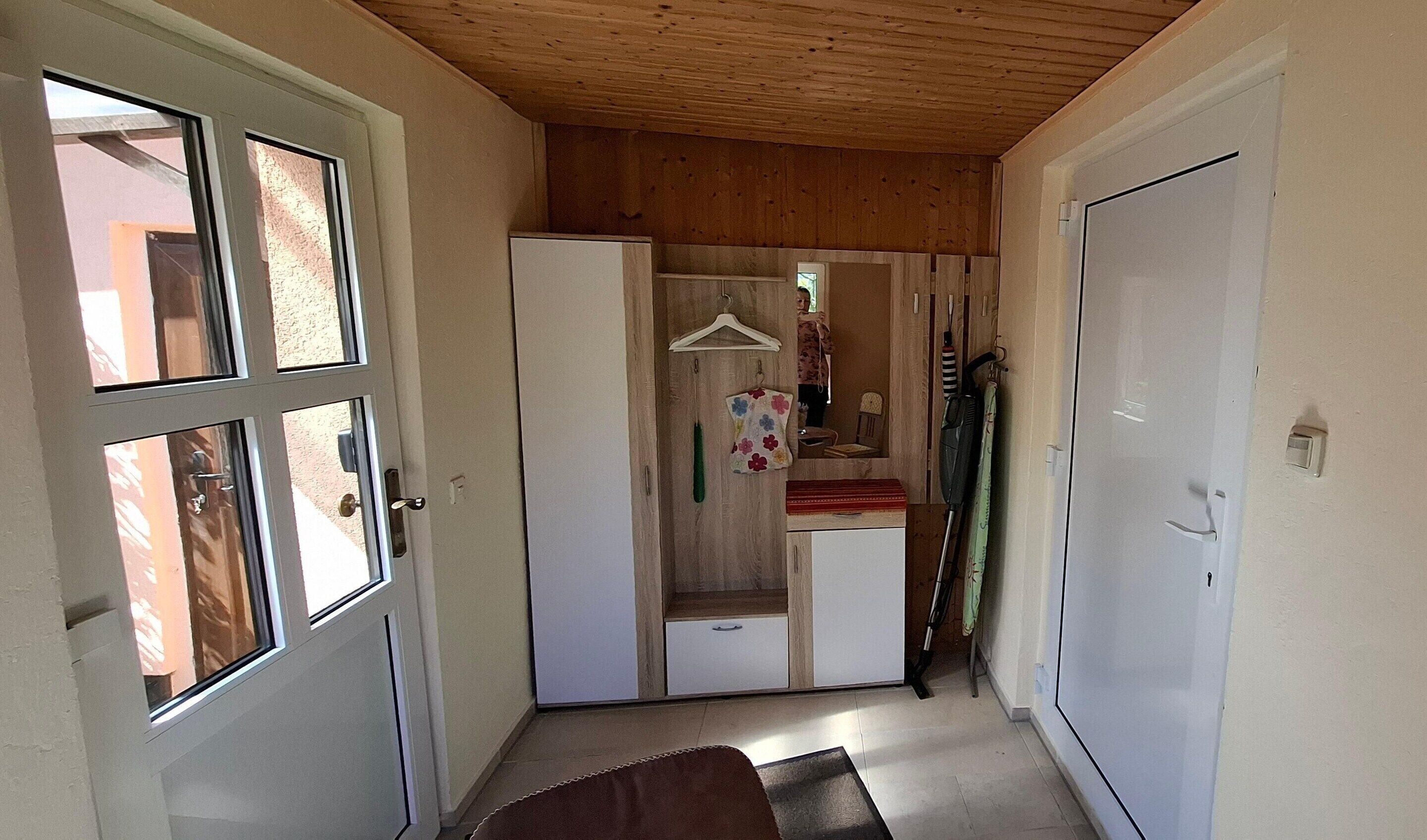 A narrow hallway with a wooden ceiling, a white door on the left, and a white wardrobe with a hanging rack in the center.