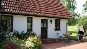 Een huis met een rood pannendak, een voordeur en een stenen terras met buitenmeubels.