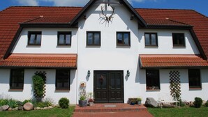 Een tweelaags huis met een rode dakbedekking, een zwarte voordeur en een groot gewei boven de ingang.