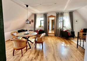 Un vaste espace de vie doté d’un plancher en bois, d’une table ronde avec des chaises, d’un canapé et d’un meuble pour la télévision.