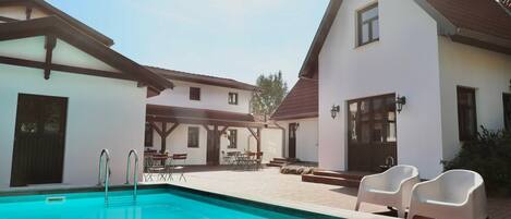 A swimming pool with a clear blue water surface, surrounded by a patio area with outdoor furniture.