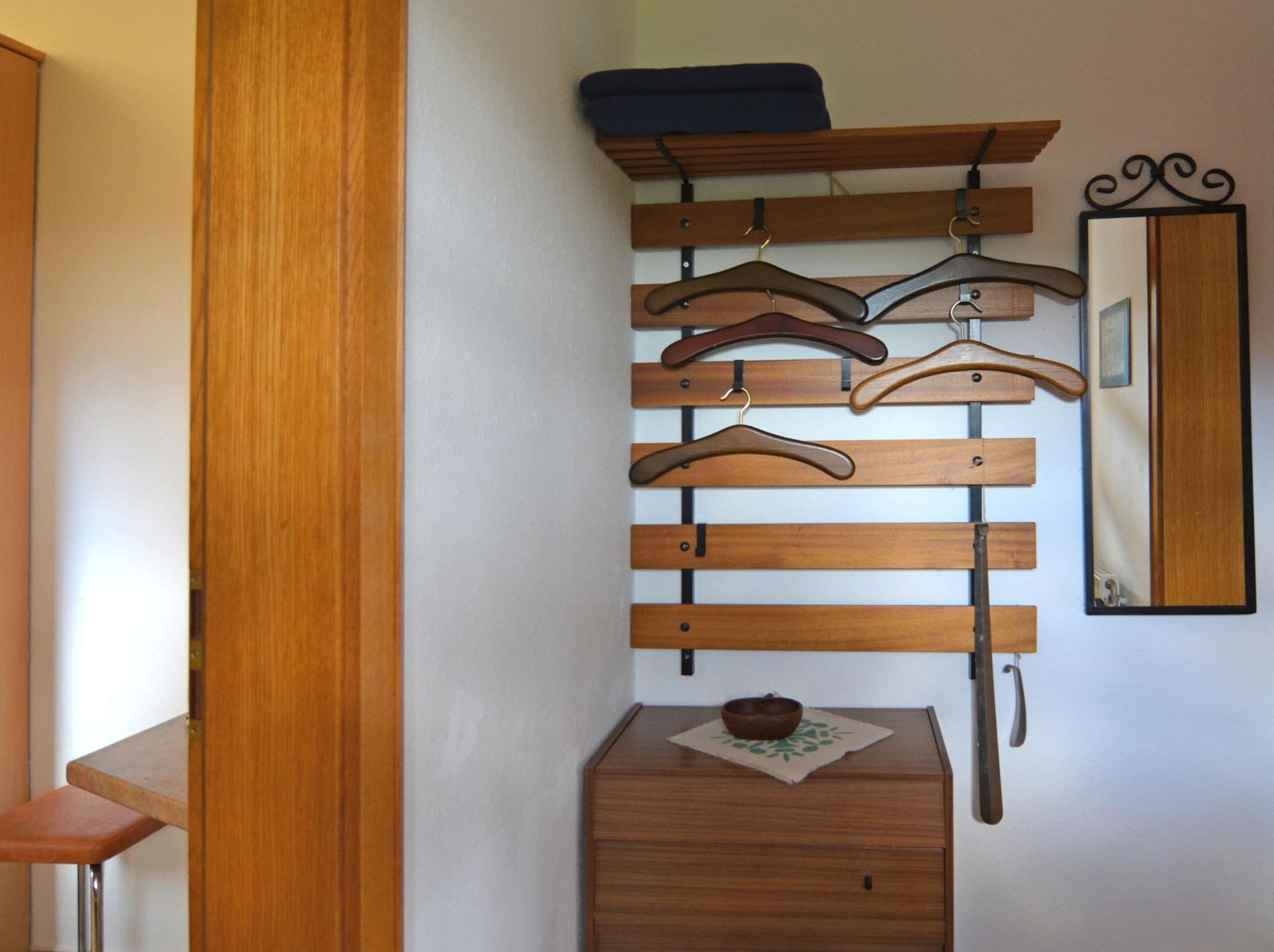 A wooden coat rack with multiple hangers, a small wooden chest, and a mirror with a decorative frame.
