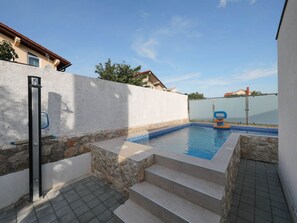 En swimmingpool med stentrapper, omgivet af en hvid mur og et hegn.