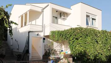 Un bâtiment moderne à deux étages, avec une façade blanche, un escalier extérieur abrité et un mur recouvert de lierre.