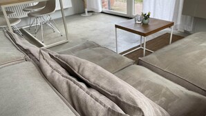 Ein modernes Wohnzimmer mit einem beigen Sofa, einem kleinen Holztisch und einem weißen Sessel.