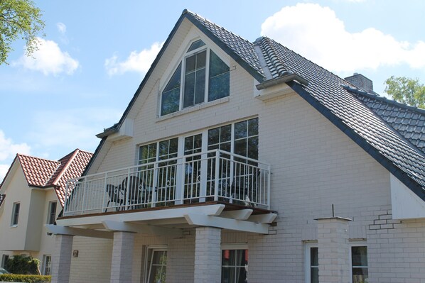 A two-story house with a balcony, large windows, and a tiled roof. - Ferienwohnung in Zingst mit Terrasse (Zingst)