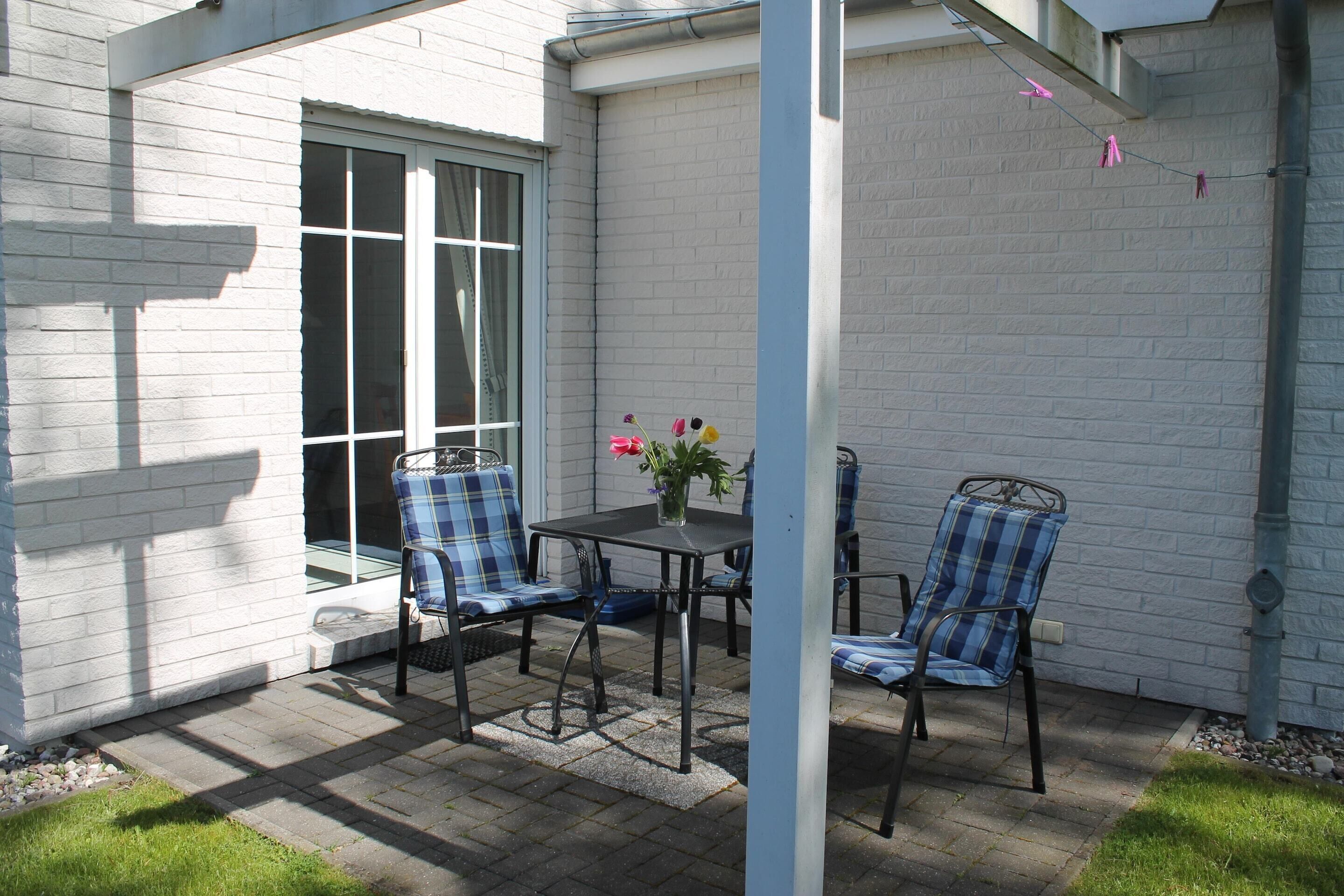 Een terras met een tafel, stoelen, een raam en een bakstenen muur.