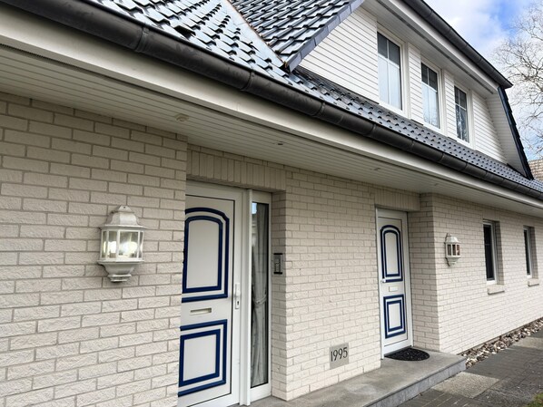 A two-story house with white brick exterior, two front doors with blue trim, and a small window on the second floor. - Ferienwohnung in Zingst mit Terrasse (Zingst)