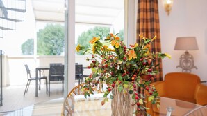 A modern living room with a glass coffee table, a vase with yellow flowers, and a view of the outdoors through large windows. - Holiday Home in Sirmione Near Thermal Baths (Sirmione)