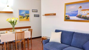 A dining area with a table set for two, a blue sofa, and a painting of a coastal scene. - Holiday Home in Sirmione Near Thermal Baths (Sirmione)
