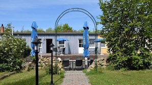Een pad dat leidt naar een terras met blauwe parasols, een stenen muur en een gebouw met een blauw luifel.