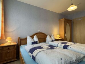 A bedroom with two beds, wooden headboards, bedside lamps, and a wardrobe.