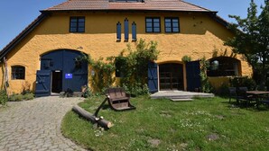 A yellow building with a tiled roof, two large arched doors, and a paved pathway leading to the entrance.