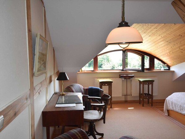 Une chambre confortable située dans les combles, avec un plafond en bois, une grande fenêtre, un bureau avec une lampe, une chaise et un lit.