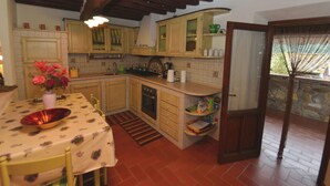 A kitchen with wooden cabinets, a tiled backsplash, a dining table with chairs, and a window with a view of greenery. - Modern Villa With Private Pool and Fenced Garden Near Lucca (Capannori)
