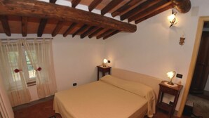 A bedroom with a bed, two bedside tables with lamps, a window with curtains, and a wooden ceiling beam. - Modern Villa With Private Pool and Fenced Garden Near Lucca (Capannori)