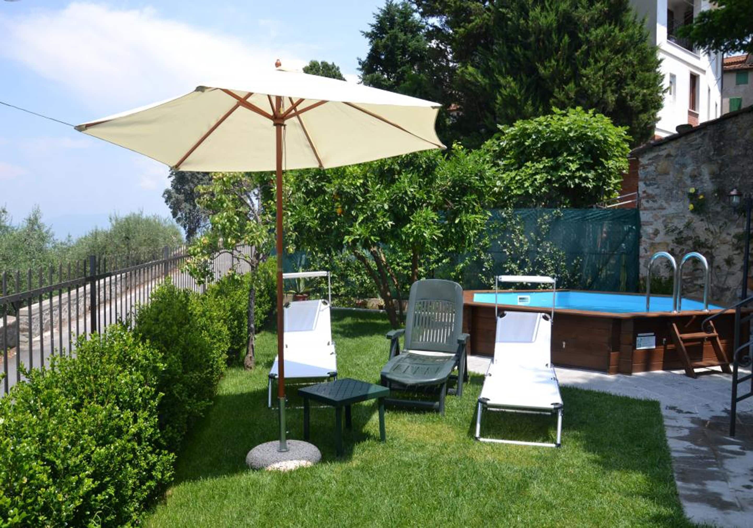A backyard with a pool, lounge chairs, and a table under a large umbrella.