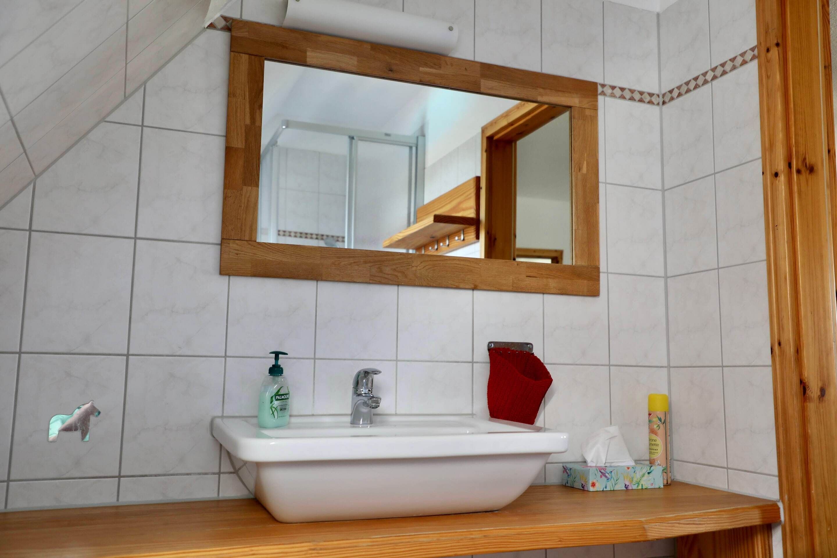Un baño con lavamanos blanco, espejo y tocador de madera.