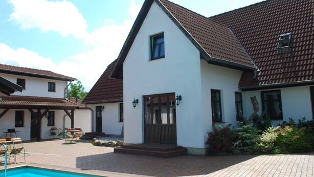 A white building with a brown roof, a swimming pool, and outdoor seating. - Spacious Retreat in Dargun (Dargun)