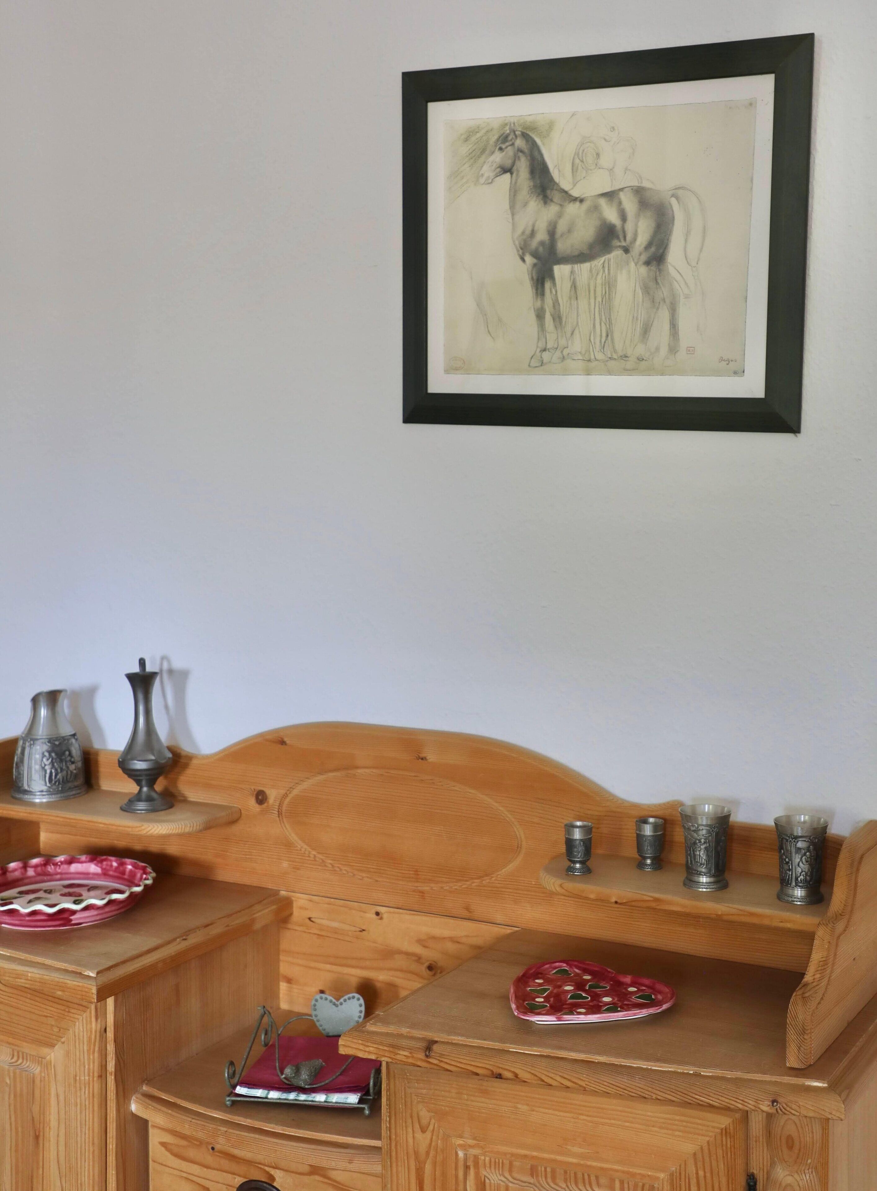 A wooden headboard with a framed drawing of a horse, a small shelf with decorative items, and a wooden cabinet with a red plate and a heart-shaped ornament.