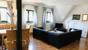 A living room with a dark sofa, a dining table with chairs, and a chandelier. - Spacious Retreat in Dargun (Dargun)