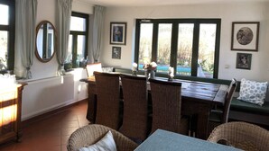 A dining area with wicker furniture, a table, and chairs. There are windows with curtains, a radiator, and framed pictures on the wall. - Spacious Retreat in Dargun (Dargun)