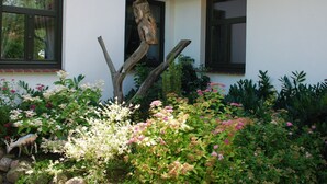 A house with two windows, a wooden sculpture, and a garden with various plants and flowers. - Spacious Retreat in Dargun (Dargun)