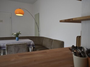 A dining area with a table, chairs, a vase with flowers, a lamp, and a wooden counter with utensils.
