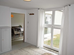 A room with a large window, a dining area with a table and chairs, and a white wardrobe.