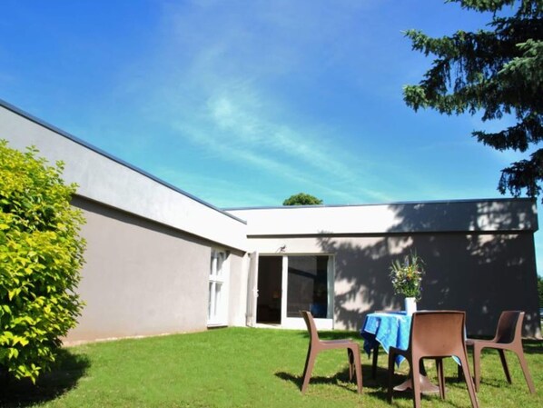 A modern building with a flat roof, a grassy yard, and a patio area with a table and chairs.