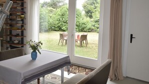 En matplats med ett bord dukat för två personer, en blå vas med blommor och utsikt över en trädgård genom glasdörrar.