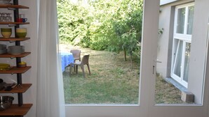 Ett rum med en dörr som leder ut till en trädgård med ett bord och stolar, samt hyllor med köksredskap.