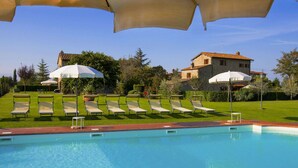 A swimming pool with lounge chairs and umbrellas, surrounded by a well-maintained lawn and stone buildings.