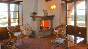 A cozy living room with a fireplace, wicker chairs, a glass coffee table, and a view of the outdoors.