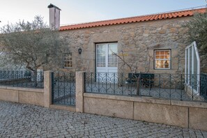 Un bâtiment en pierre avec un toit en tuiles, une clôture en métal et un chemin pavé.