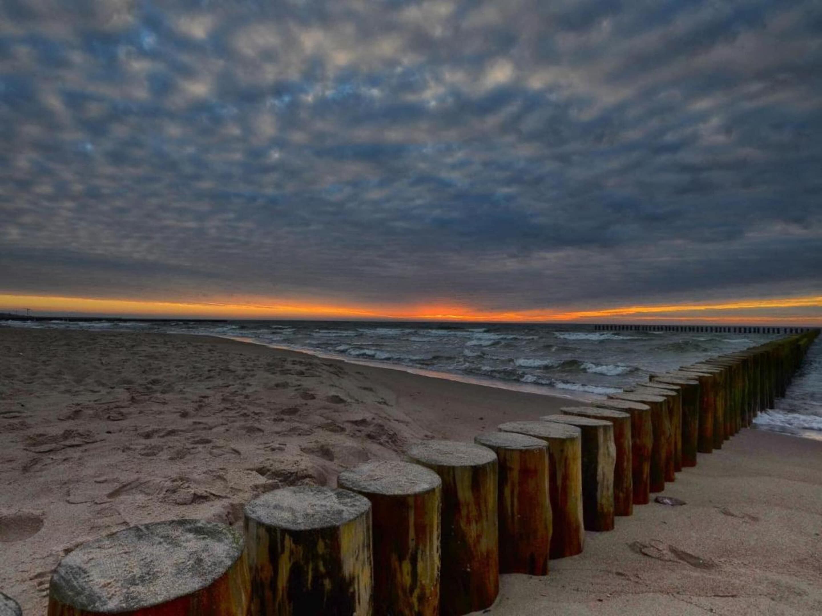 A beach with a wooden groyne and a cloudy sky.