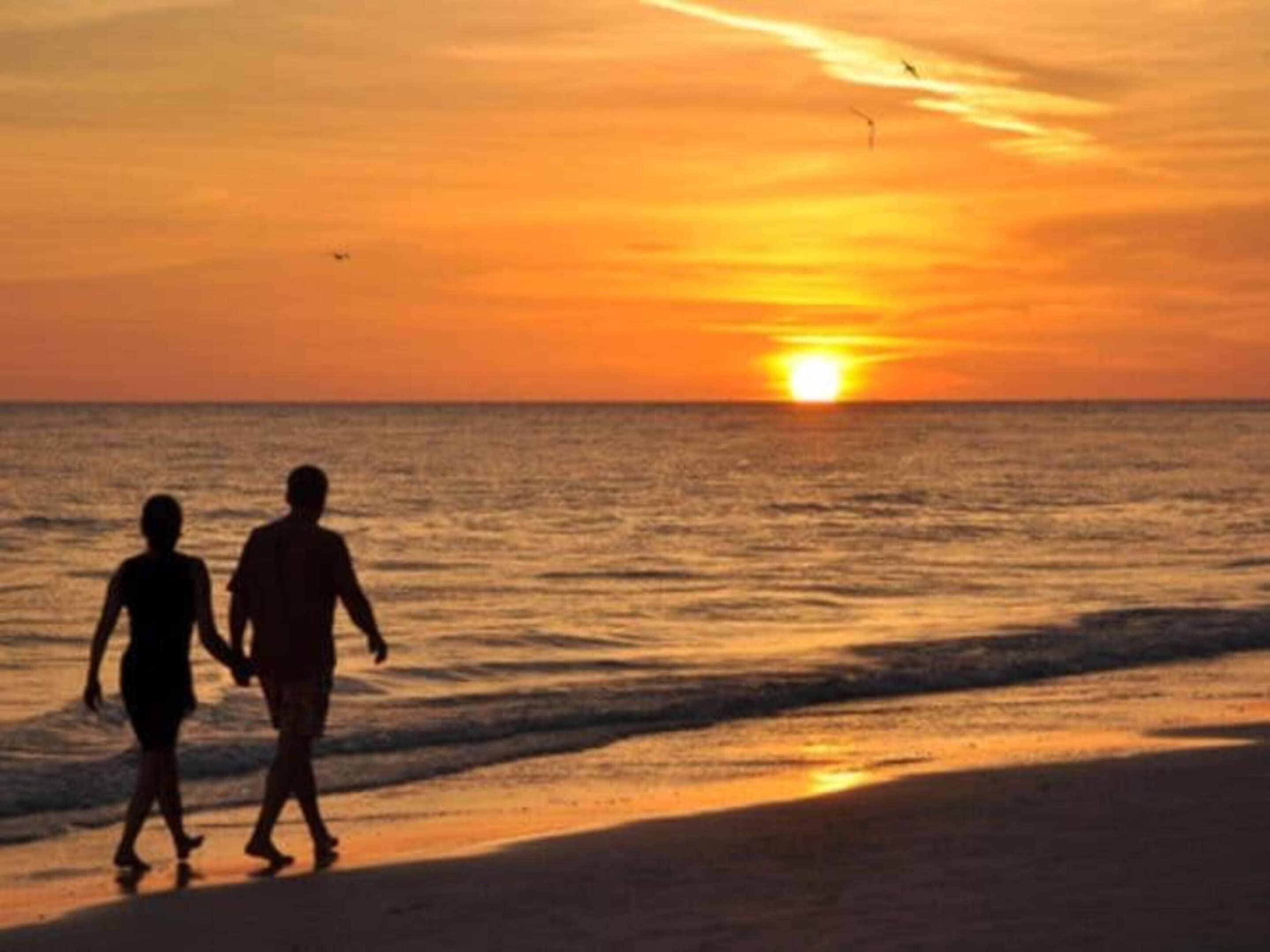 Zwei Personen laufen am Strand während des Sonnenuntergangs.